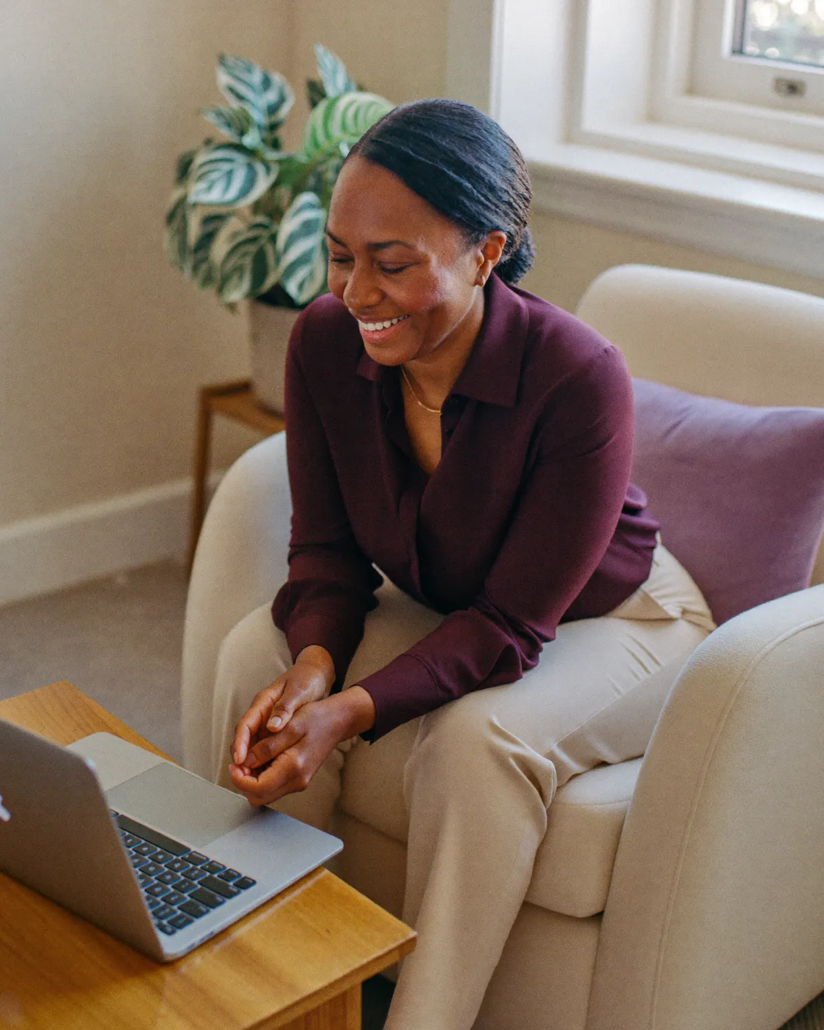 A smiling counsellor in a cream armchair beside a laptop, ready for an online session