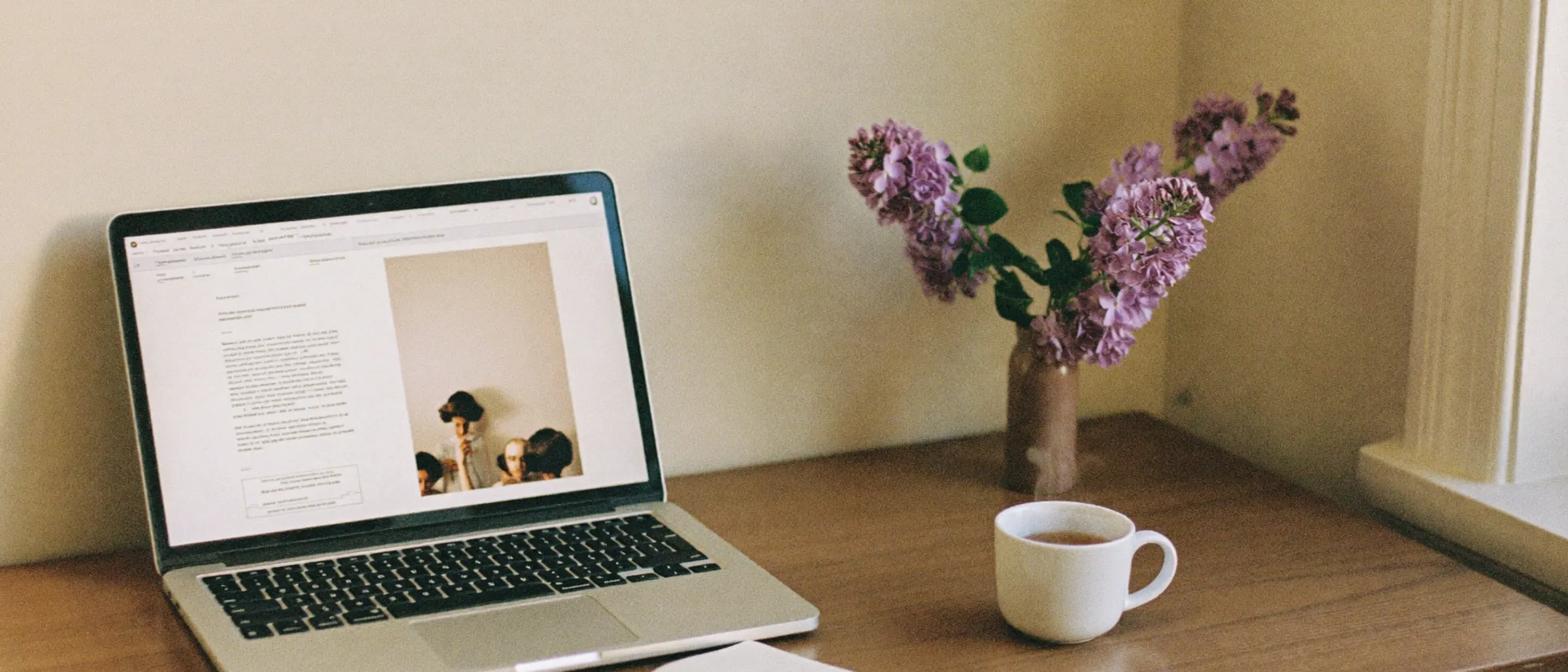 A laptop open on a table beside a cup of tea in a softly lit room
